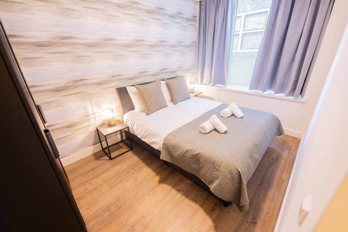 A bedroom with a bed, pillows, a nightstand with a lamp, and a window with curtains.
