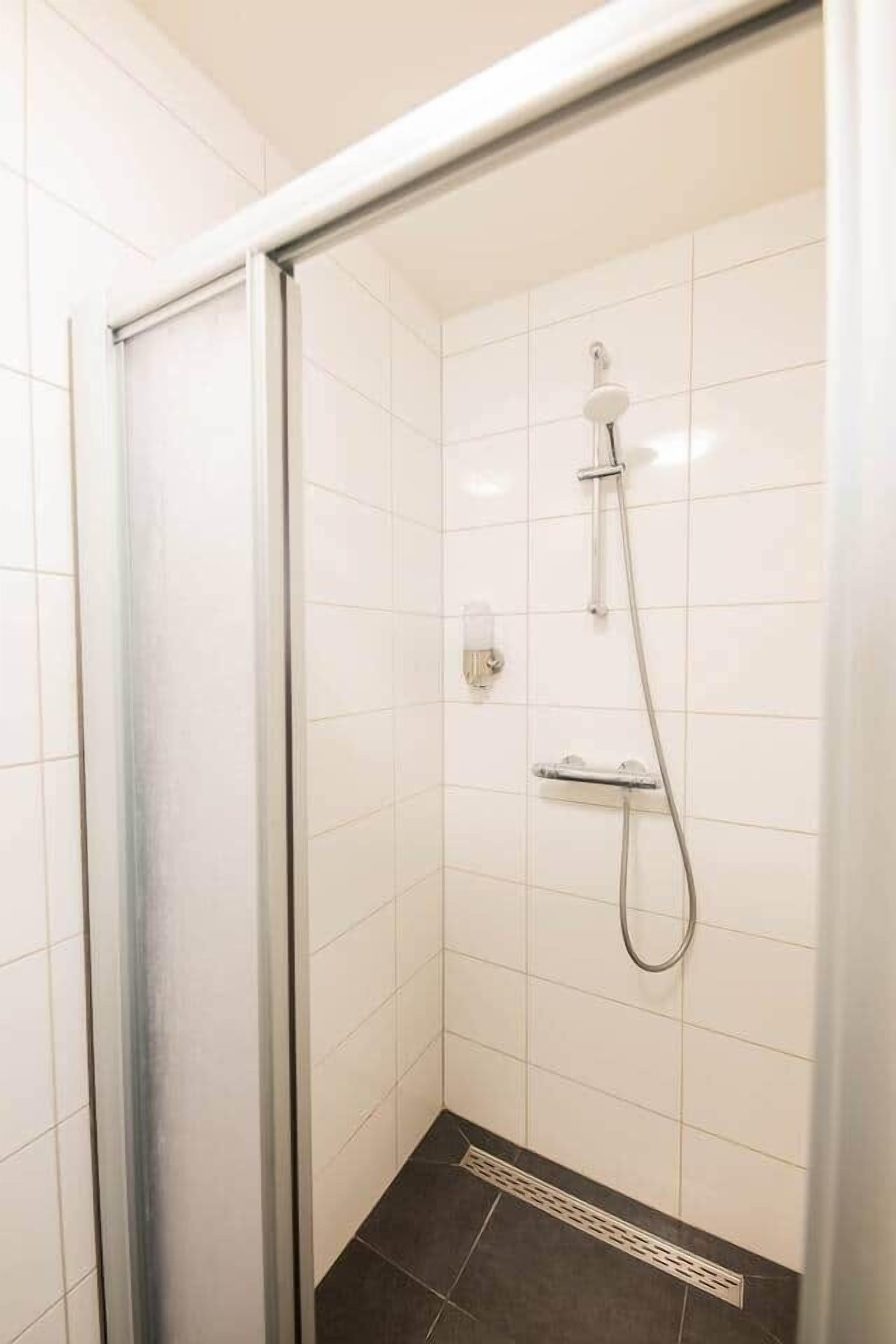 Un angolo doccia con porta in vetro, pareti piastrellate di bianco e soffione.