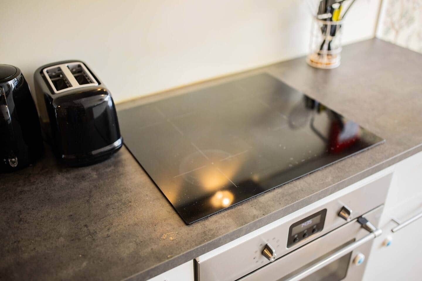 A kitchen with a black induction cooktop, a toaster, and a coffee maker on the countertop.