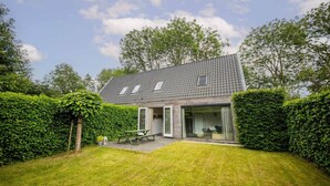 Une maison avec un toit en pente, une terrasse avec une table et des chaises, et un jardin bien entretenu.