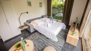A modern hotel room with a bed, a desk, a chair, a lamp, and a large window with curtains. - Superb 90m² Apartment with Garden (KS-8-A) (Eindhoven)