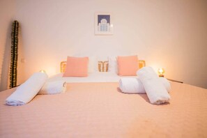 A hotel room with a bed, pillows, a framed picture on the wall, and a lamp on the nightstand.