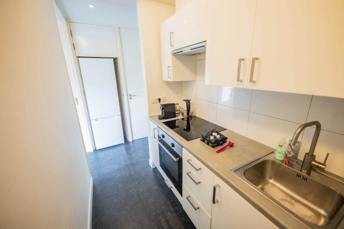 Een compacte keuken met een RVS spoelbak, een kookplaat en een klein aanrecht.