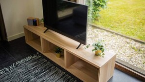 A flat-screen TV on a wooden TV stand with shelves, a small plant, and a remote control. - Superb 90m² Apartment with Garden (KS-8-A) (Eindhoven)
