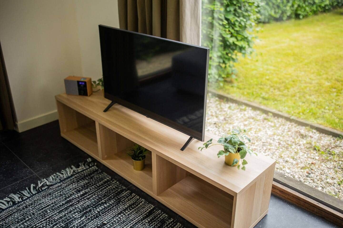 Un televisor de pantalla plana sobre un mueble de madera con estantes, una planta pequeña y un control remoto.