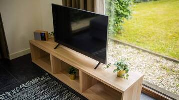 Un televisor de pantalla plana sobre un mueble de madera con estantes, una planta pequeña y un control remoto.