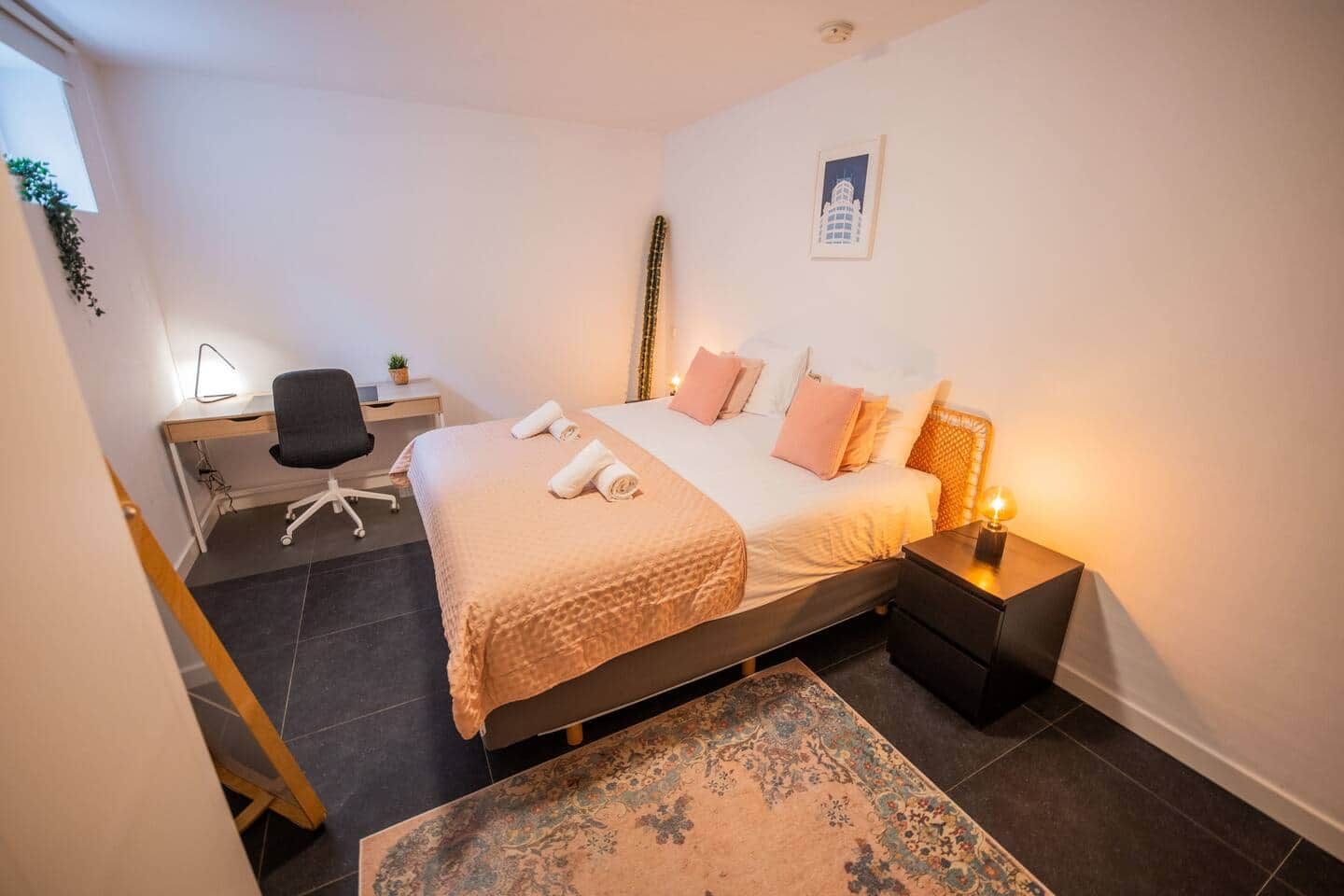 Een slaapkamer met een bed, nachtkastjes, een bureau, een stoel en een vloerkleed.