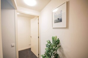 Um corredor com uma porta, um quadro na parede e um vaso de planta.