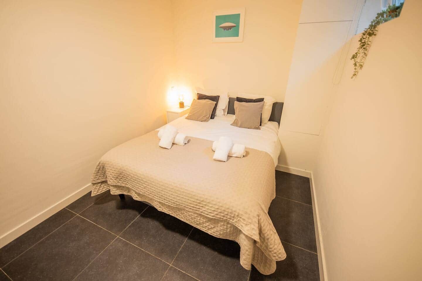 A neatly made bed with a blanket and towels, a bedside lamp, and a framed picture on the wall.
