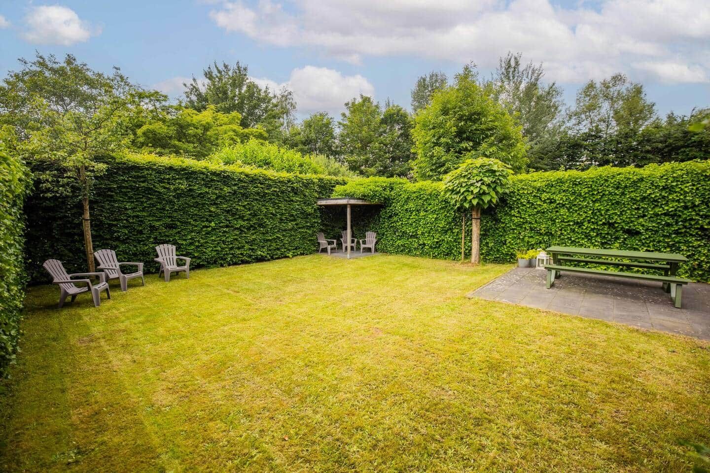 Ein gepflegter Garten mit einem Lauben, einer Sitzgelegenheit und einer Bank.