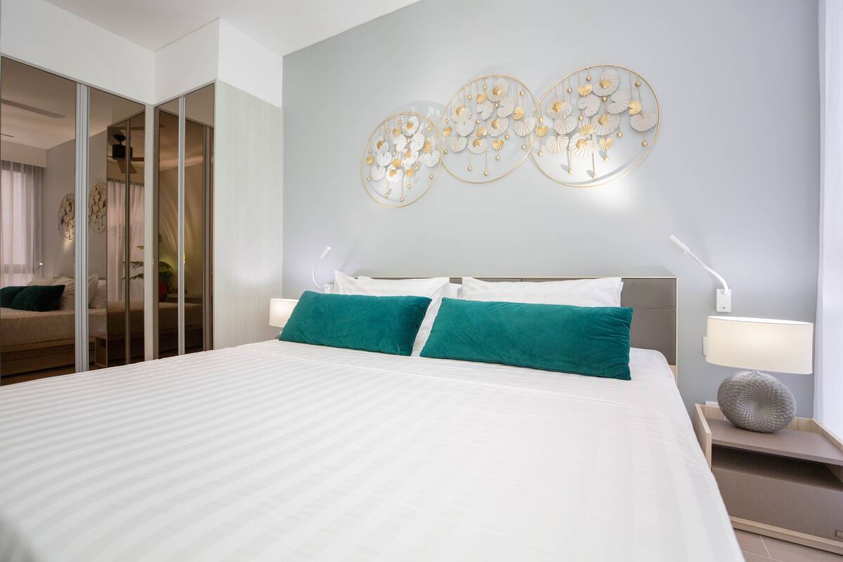 A modern bedroom with a large bed, teal pillows, a bedside lamp, and a wall art piece.