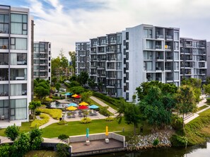 A modern multi-story residential building with balconies, a landscaped garden, and a small pond.