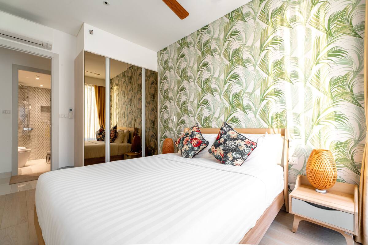 A bedroom with a bed, a nightstand, a lamp, and a shower area.