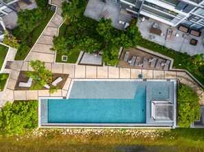 An aerial view of a modern hotel with a swimming pool, outdoor seating, and lush greenery.