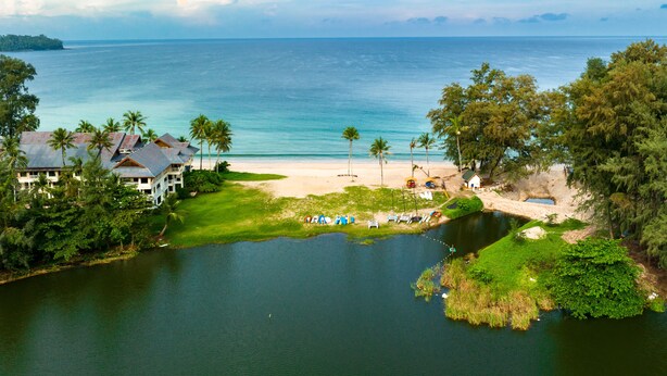 A coastal resort with a beach, a small lake, and a few palm trees. - Cassia Residences by NLA (Choeng Thale)