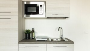 Una cocina moderna con un microondas de acero inoxidable, un lavamanos con grifo y una pequeña planta en maceta.