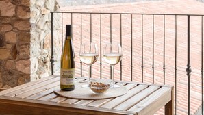 Una botella de vino y dos copas sobre una mesa de madera con vista a un camino de ladrillo y un muro de piedra.