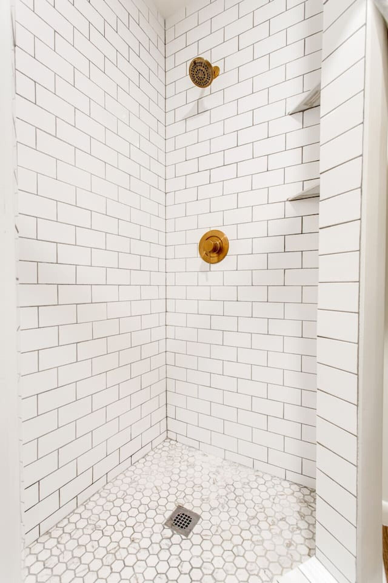 Une douche d’angle avec des carreaux de métro blancs et un sol recouvert de carreaux hexagonaux.