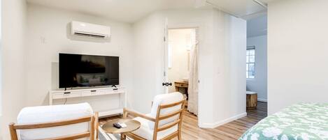 A hotel room with a bed, a TV, a ceiling fan, and a small table with chairs.