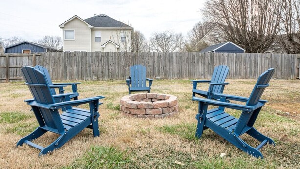 Patio trasero con tres sillas Adirondack dispuestas alrededor de un hogar de piedra.