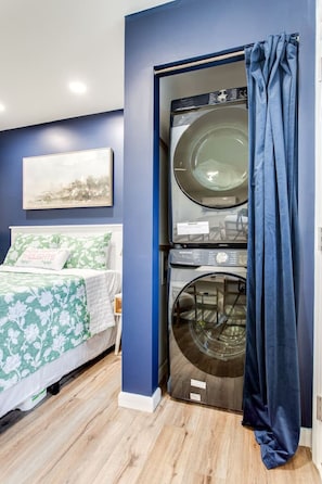 Un dormitorio con cama, lavadora y una cortina azul.