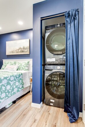 A bedroom with a bed, a washing machine, and a blue curtain.