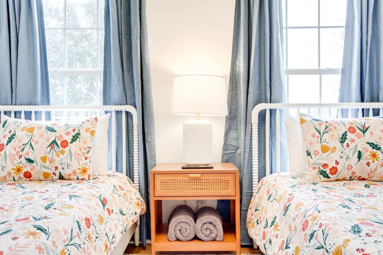 Une chambre avec deux lits, une table de chevet avec une lampe et une fenêtre avec des rideaux.