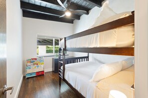 Quarto com beliche, ventilador de teto, janela com vista e estante com livros infantis.