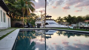 Una piscina con il riflesso di palme e uno yacht ormeggiato nelle vicinanze.