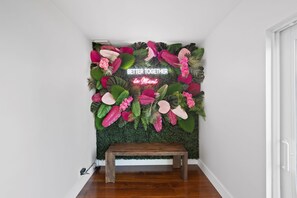 A room with a wall decorated with tropical foliage and a neon sign that reads "BETTER TOGETHER in Miami." A wooden bench is placed in front of the wall. - Waterfront Pool I Dock, Paddleboards, & Fishing (Miami)