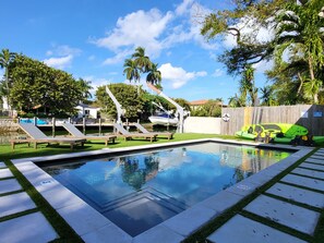 Piscina com deck de madeira, espreguiçadeiras e um caiaque verde.