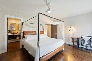 A four-poster bed with a canopy, a desk with a chair, and a ceiling fan in a hotel room.