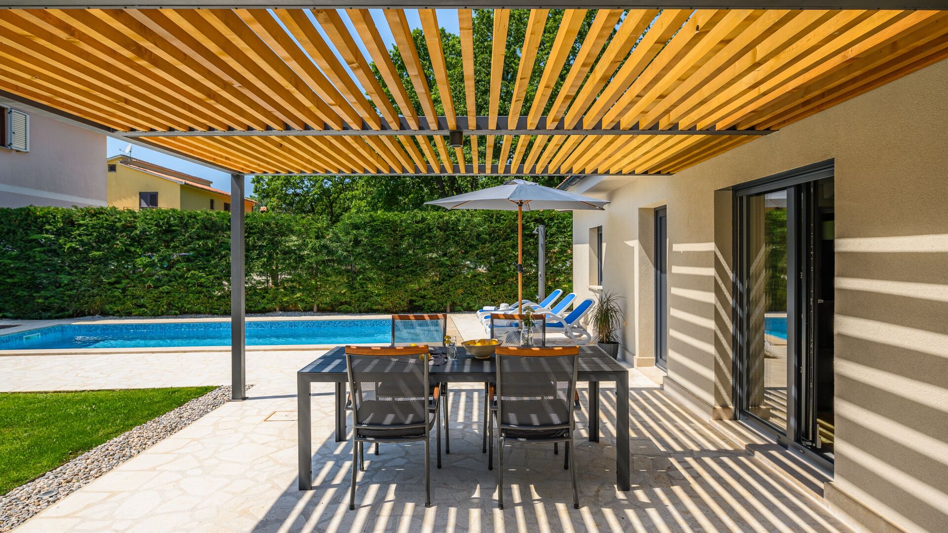 An outdoor patio with a pool, a table with chairs, and a pergola overhead.