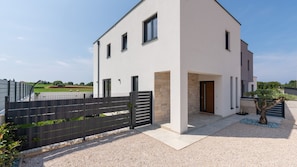 Ein modernes, zweistöckiges Haus mit flachem Dach, geschlossenem Eingangsbereich und einem kleinen Garten.