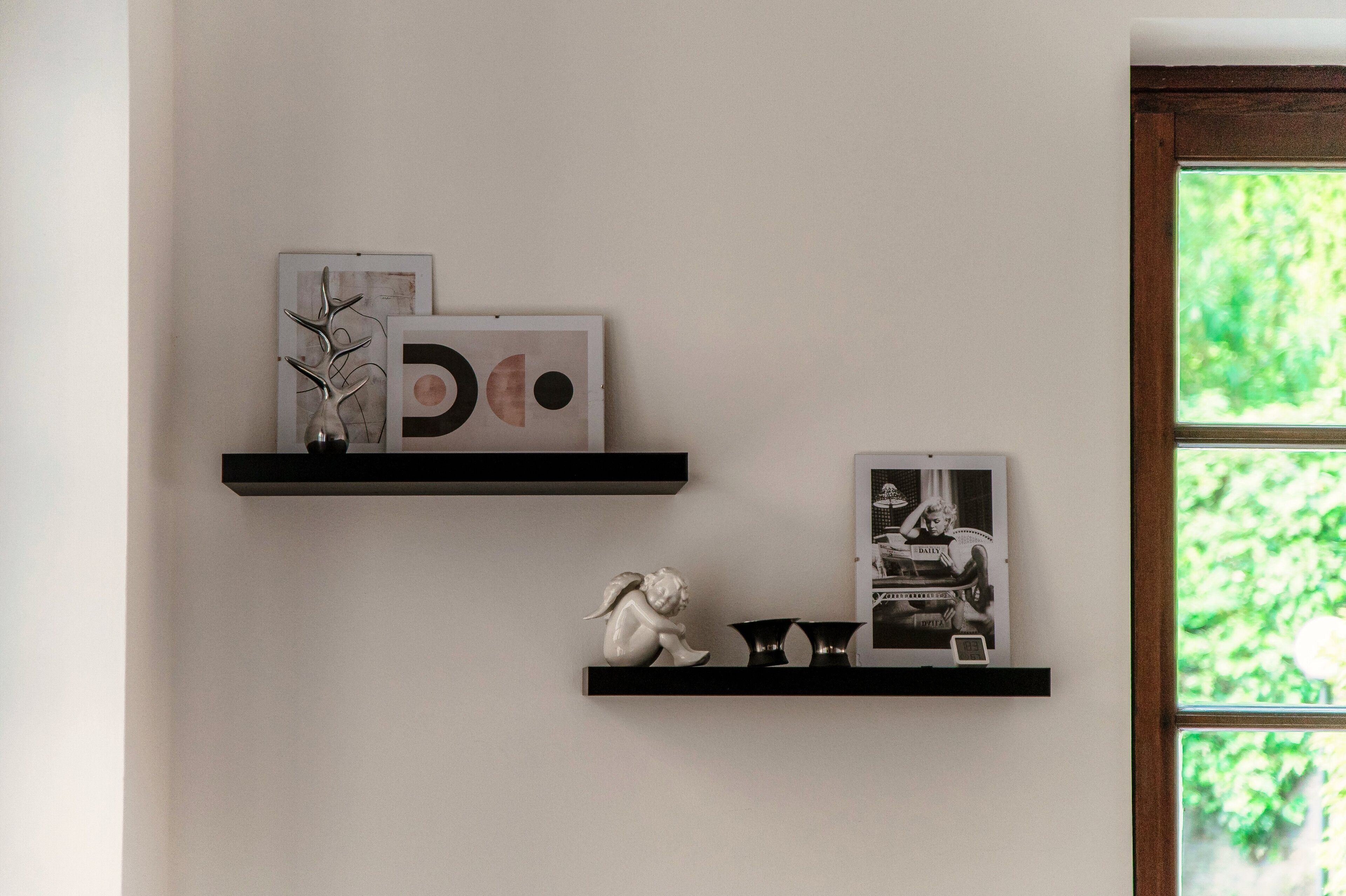 Una pared con tres estantes negros mostrando diversos objetos decorativos.