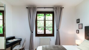 A bedroom with a bed, a desk with a chair, a window with curtains, a radiator, and a nightstand with a lamp. - Monsignor Houses (Menaggio)