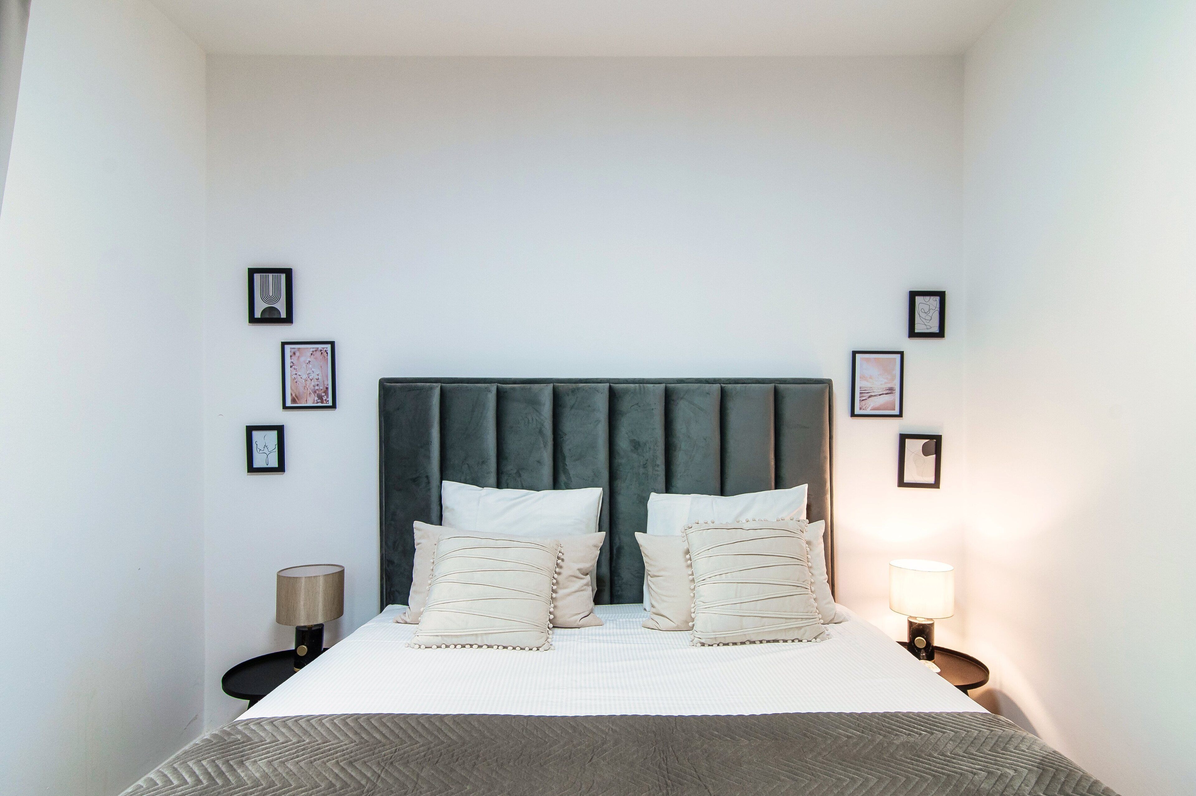 A neatly made bed with a grey headboard, two bedside lamps, and framed pictures on the walls.