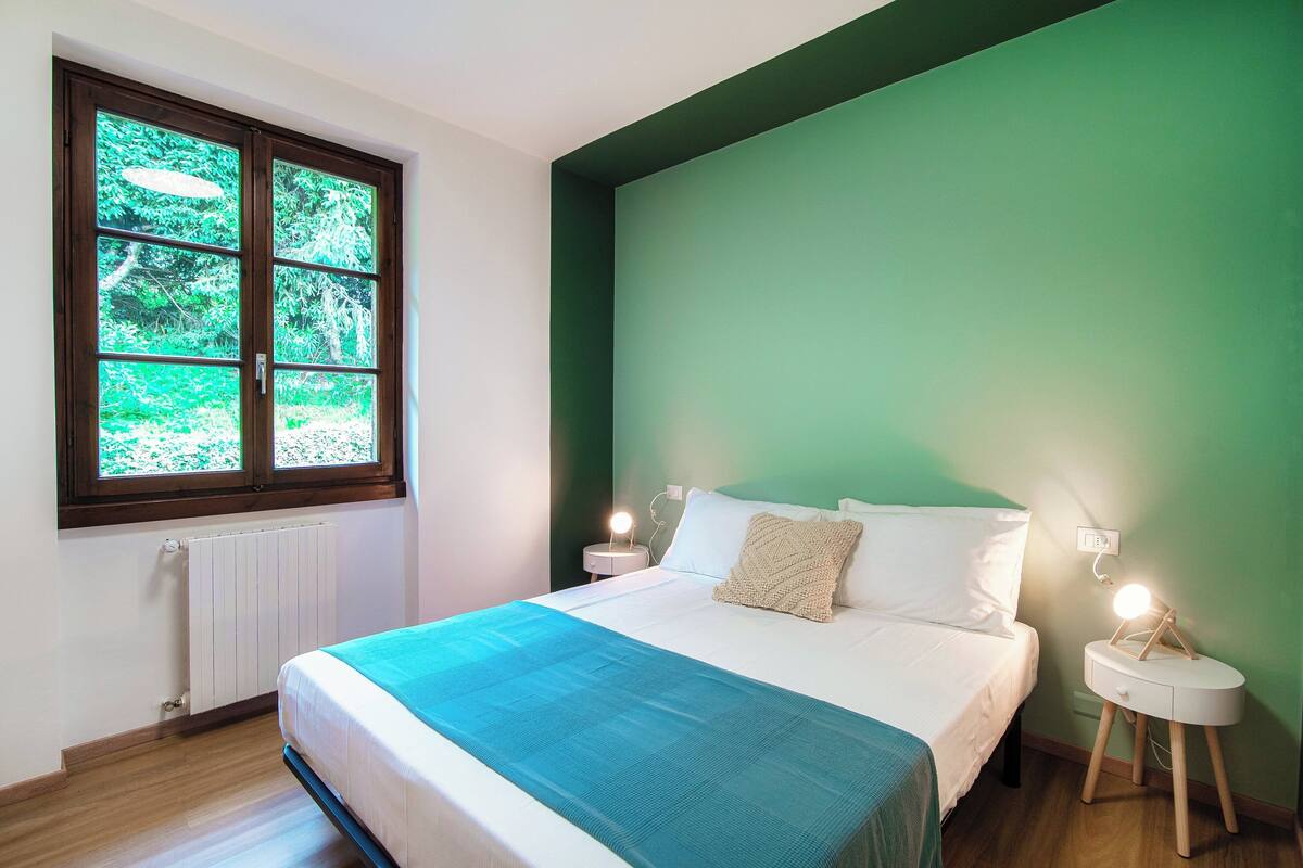 A bedroom with a bed, a nightstand, a window, and a green wall.