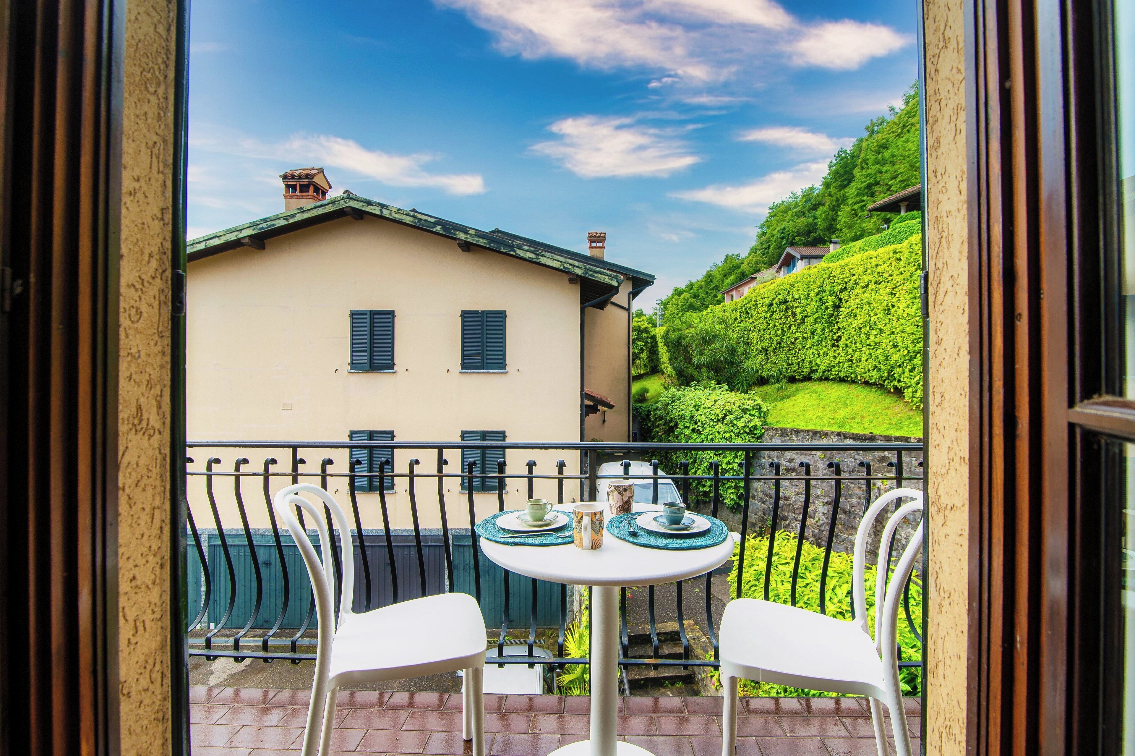 A balcony with a table and chairs, overlooking a house and lush greenery.