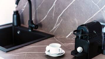 Una cocina con un lavamanos negro, una cafetera y una taza blanca sobre una encimera de mármol.