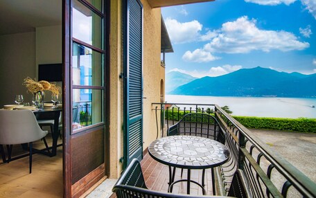 A balcony with a table and chairs, overlooking a lake and mountains.