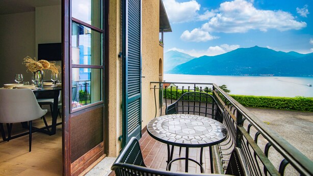 A balcony with a table and chairs, overlooking a lake and mountains. - Monsignor Houses (Menaggio)