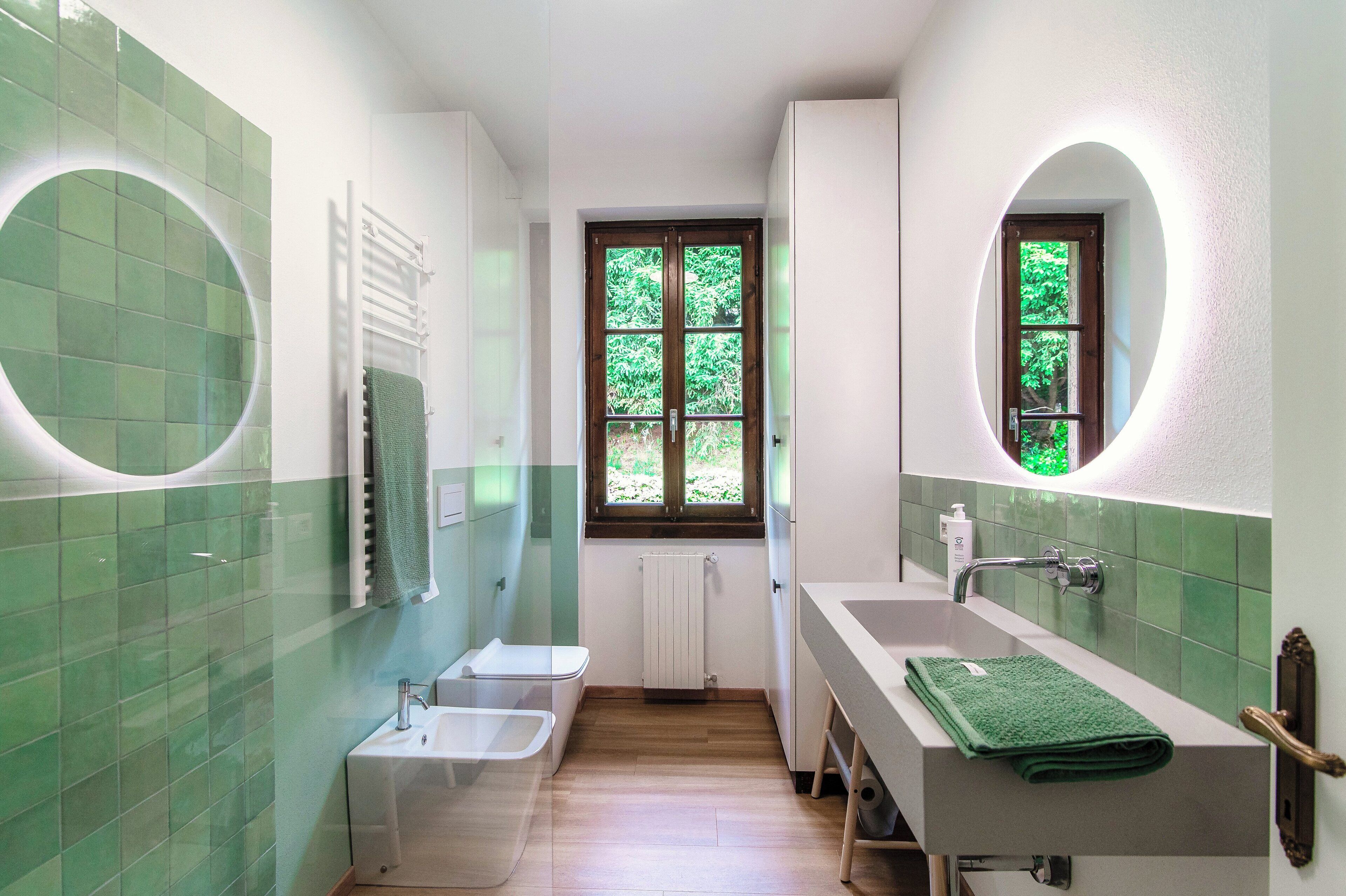 Un baño con un lavabo blanco, un espejo, un perchero para toallas y una ventana con vistas a la vegetación.