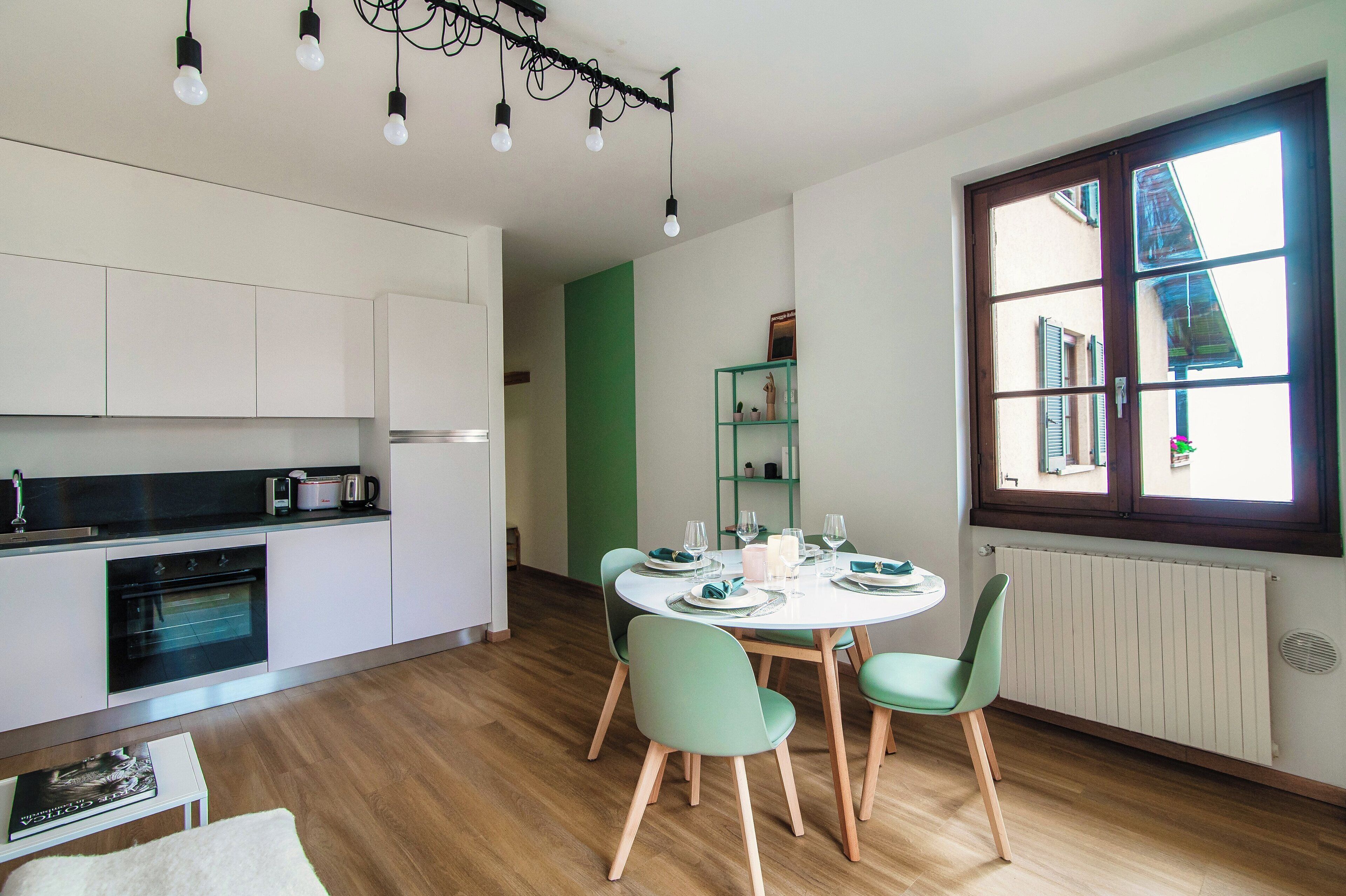 A modern kitchen with white cabinets, a built-in oven, and a dining area with a round table and green chairs.