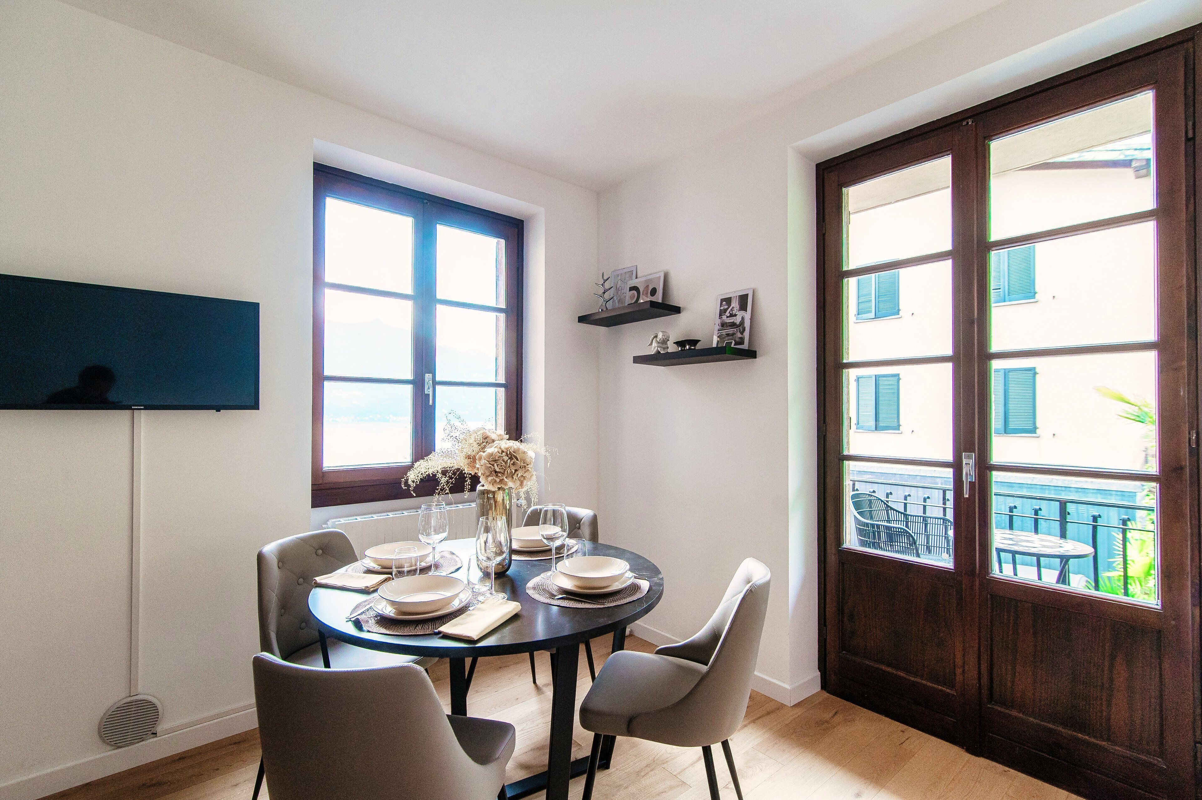 A dining area with a round table set for four, a vase with flowers, and a window with a view of buildings.