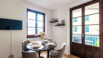 Un comedor con una mesa redonda preparada para cuatro, un florero con flores y una ventana que da a vistas de edificios.