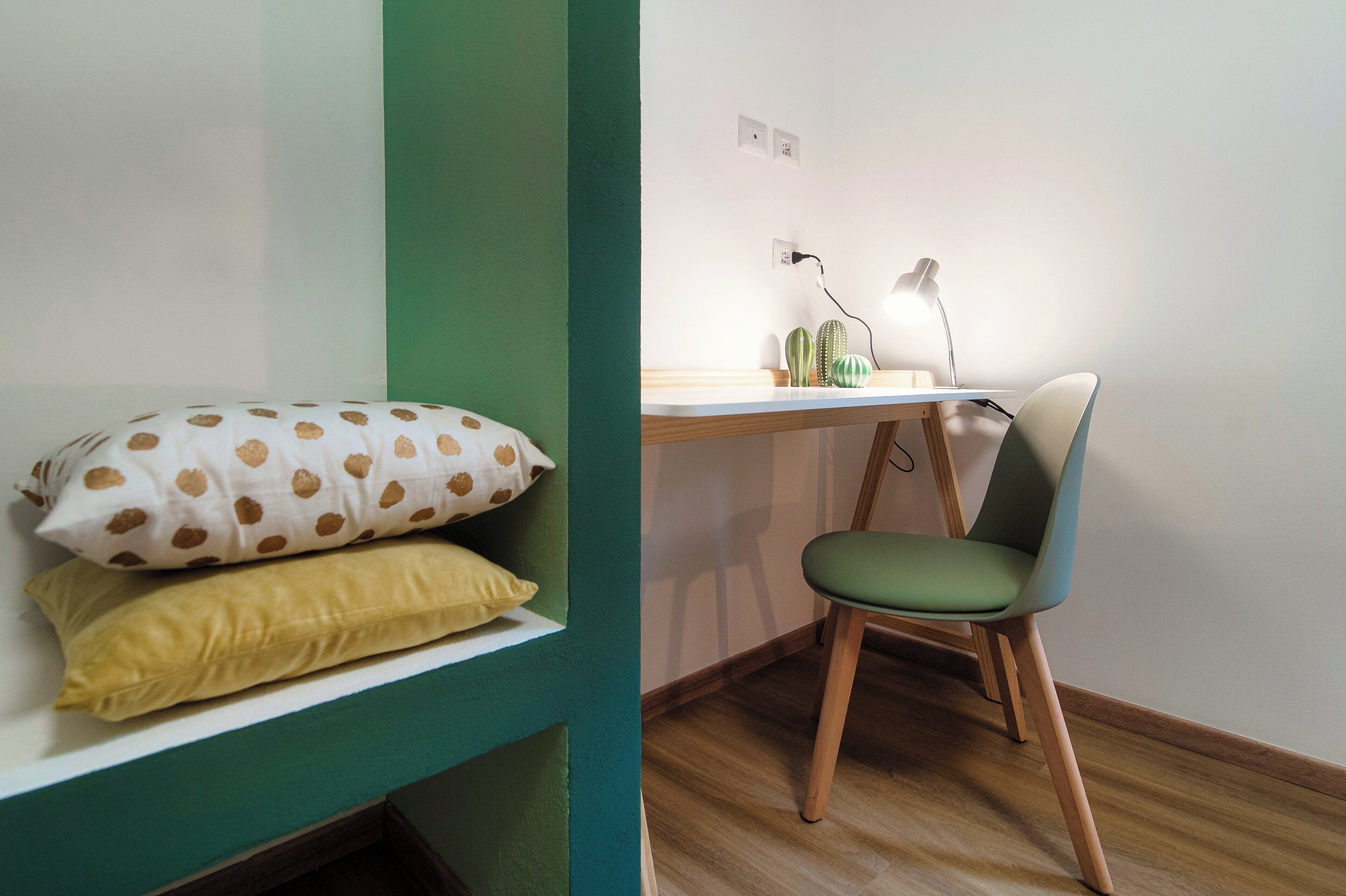 A room with a bed, a desk with a lamp, and a chair.