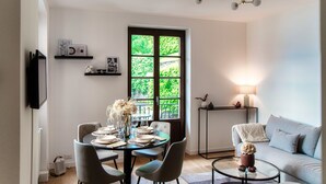 A dining area with a table set for four, a sofa, a TV mounted on the wall, and a window with a view of greenery. - Monsignor Houses (Menaggio)