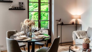A dining area with a table set for four, a window with a view of greenery, a side table with a lamp, and a sofa with a throw blanket. - Monsignor Houses (Menaggio)
