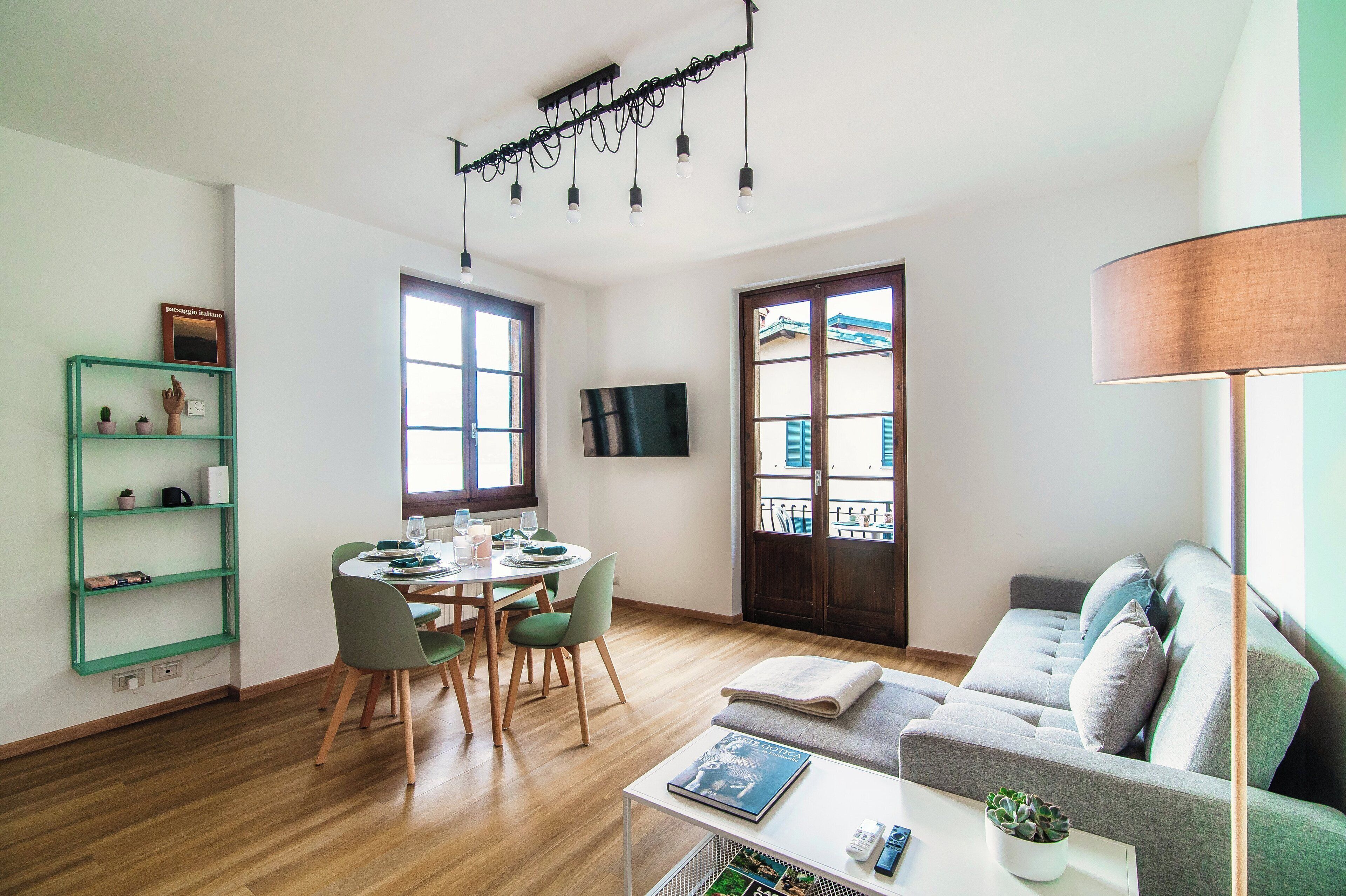 Una sala moderna con sofá, una mesa de comedor con sillas, un televisor montado en la pared y un ventanal con vistas al exterior.